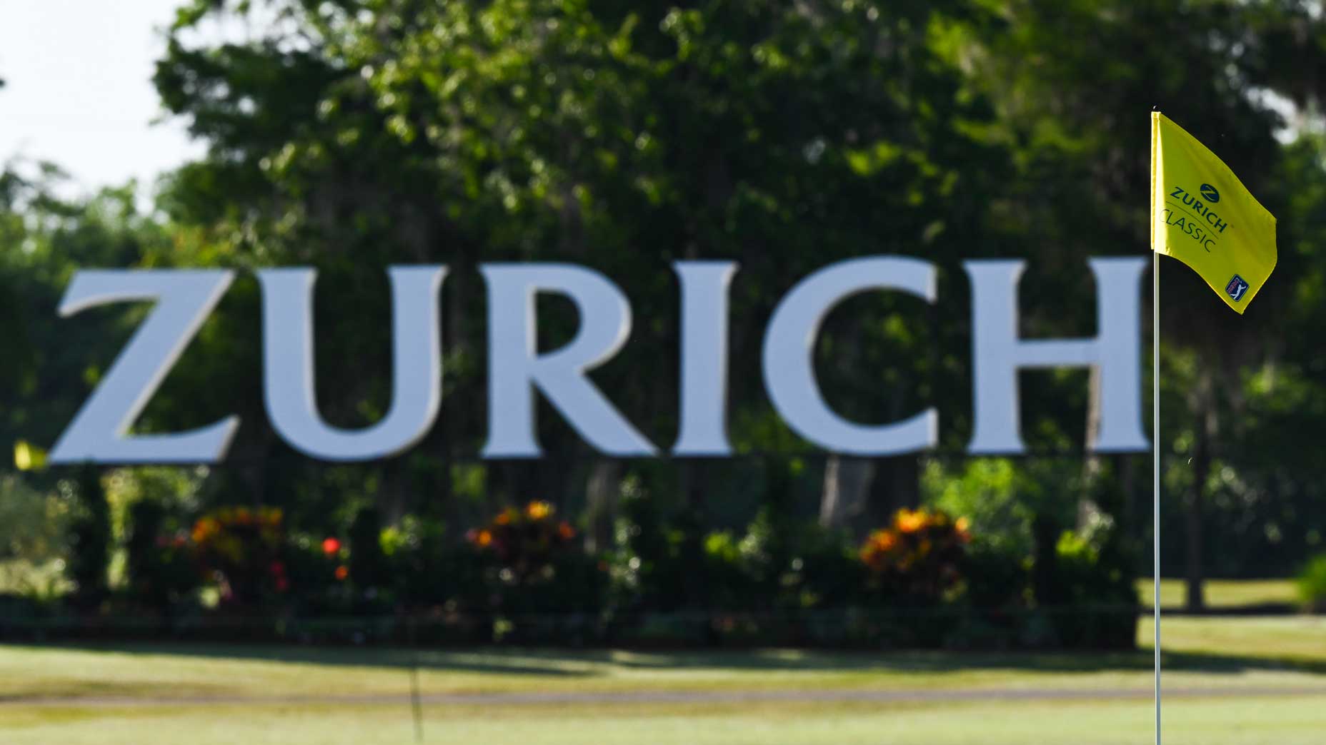A Zurich Classic sign looms in the background with a golf green and a Zurich Classic flagstick in the foreground
