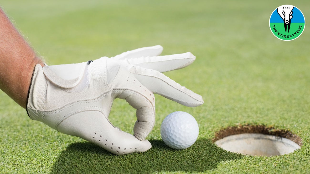 A golfer flicking a ball into the hole with his hand.