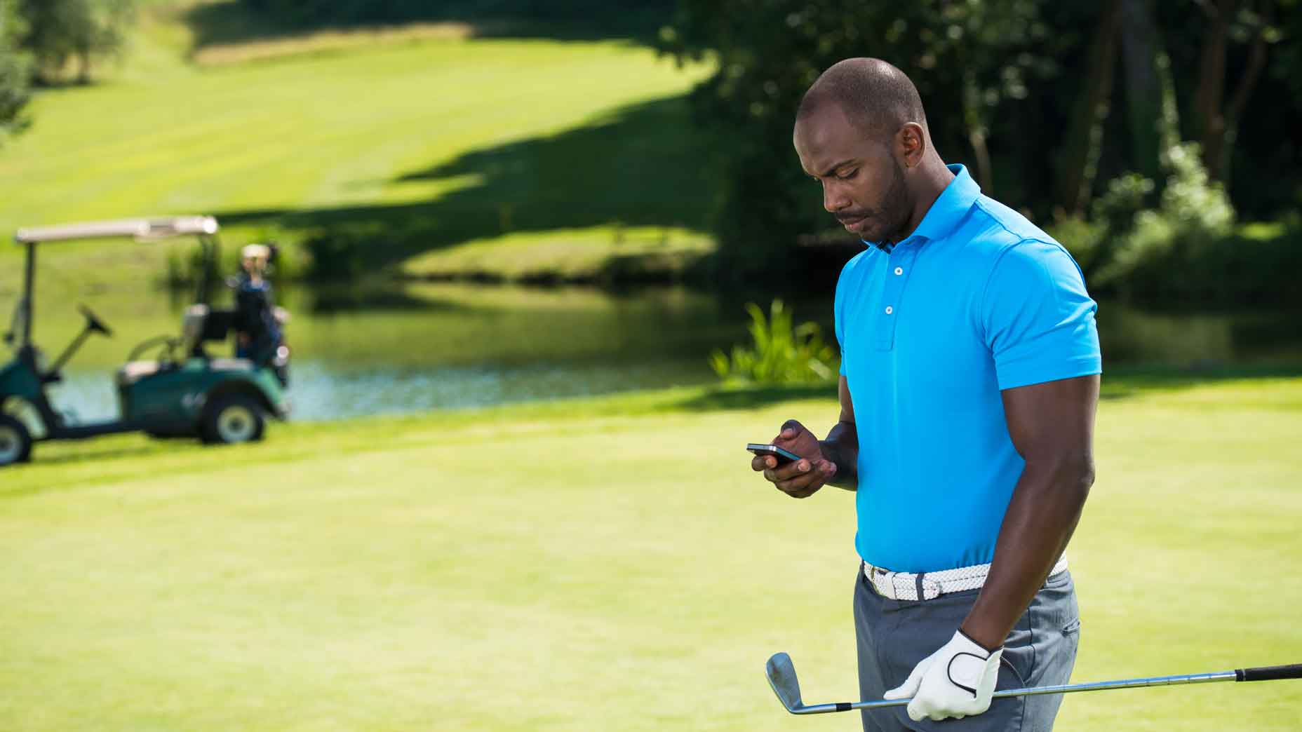 Golfer using his mobile on the course while carrying his clubs