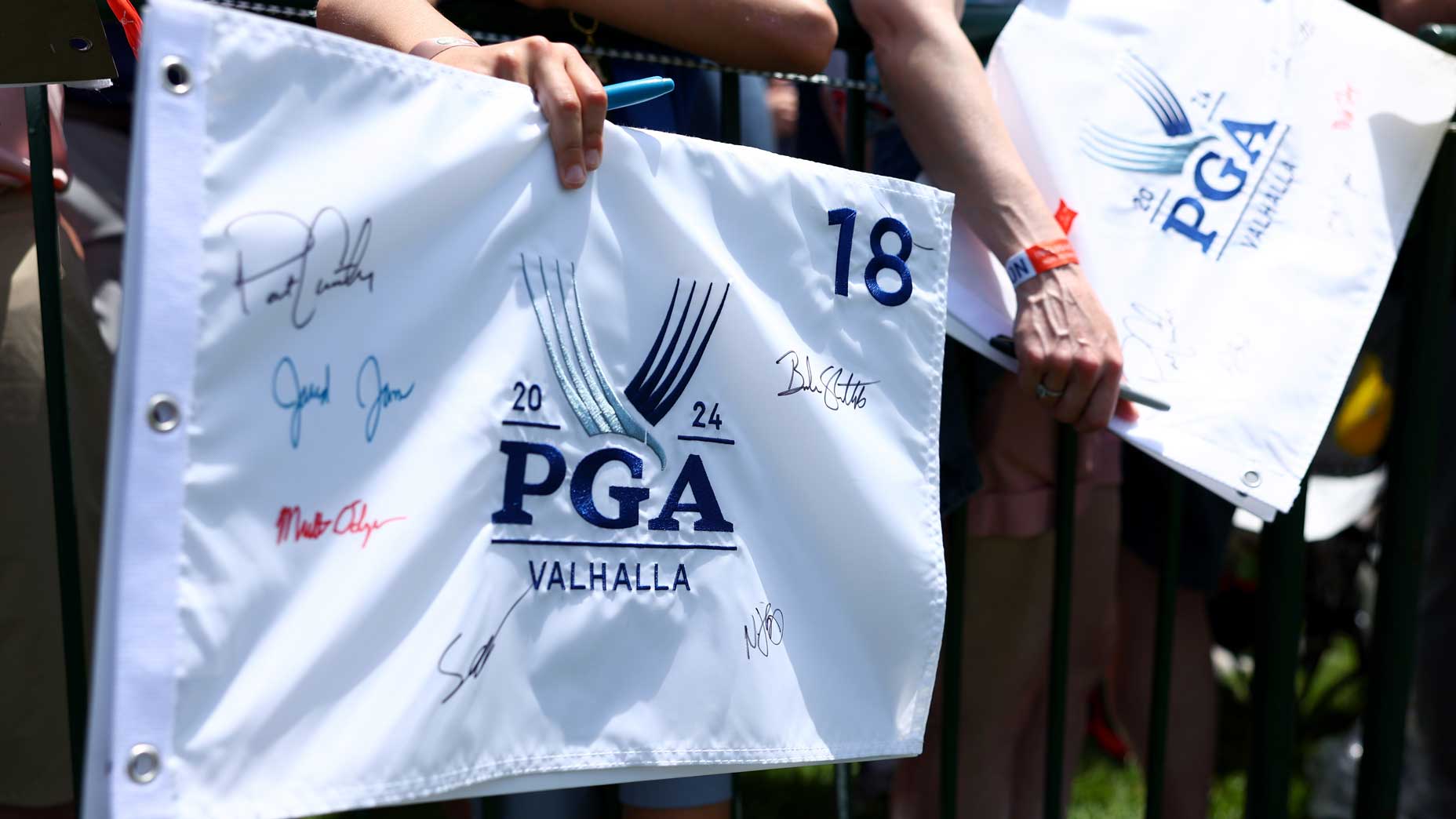 Fans hold autographed white 2024 PGA Championship flags at Valhalla