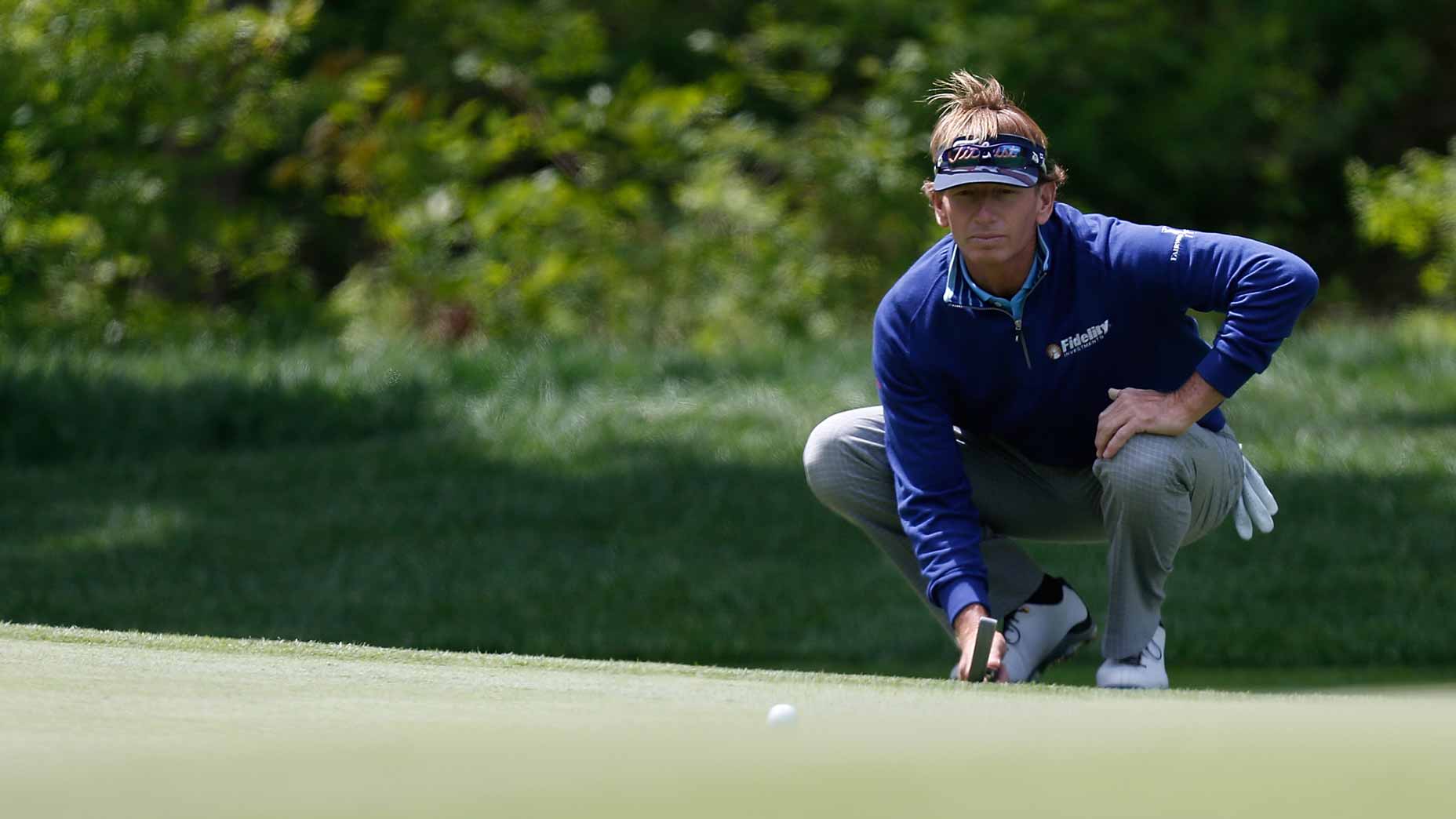 Brad Faxon crouches on golf green to read putt