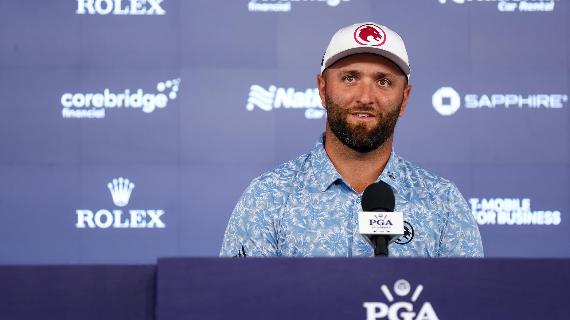 jon rahm speaks at press conference at the PGA Championship in blue shirt and red hat