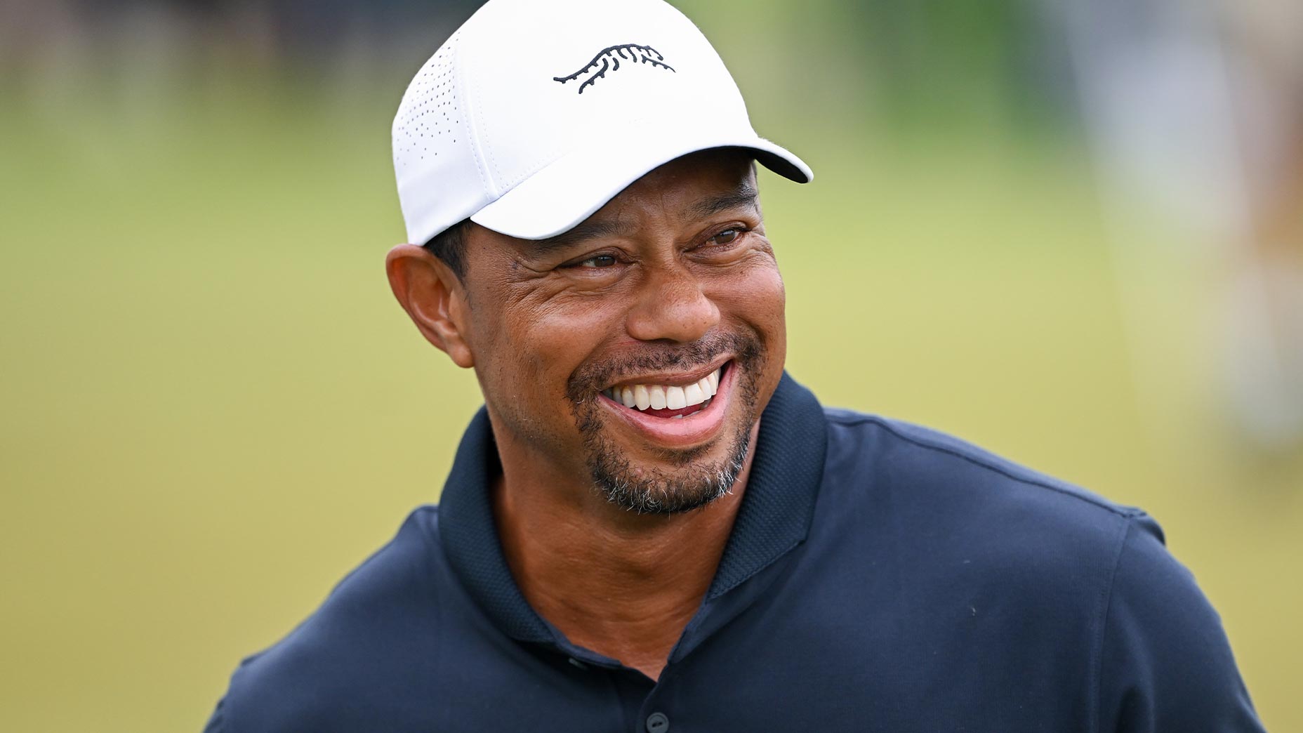 tiger woods smiles at the PGA Championship in a blue shirt and white hat