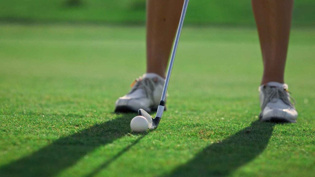 Golf player legs stand at golf course grass. Woman swinging golfing shot outside close up. Unknown professional sportswoman get ready hitting ball on fairway. Leisure exercising rich lifestyle concept