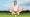 Woman golf player sitting on green in yoga posture focusing on ball dropping into cup.