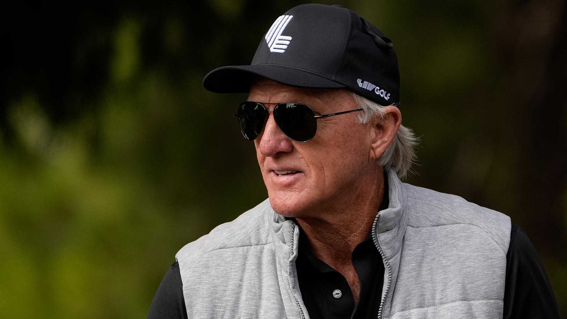greg norman stares at LIV Golf event in grey vest and black hat