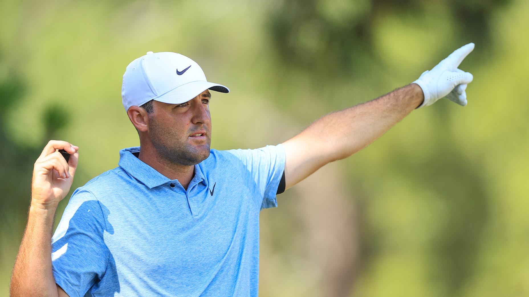 scottie scheffler points ahead of us in an open green shirt and white hat