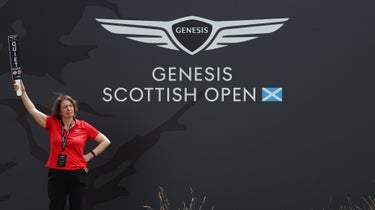 Genesis Scottish Open sign with course marshal in red shirt standing in front of it