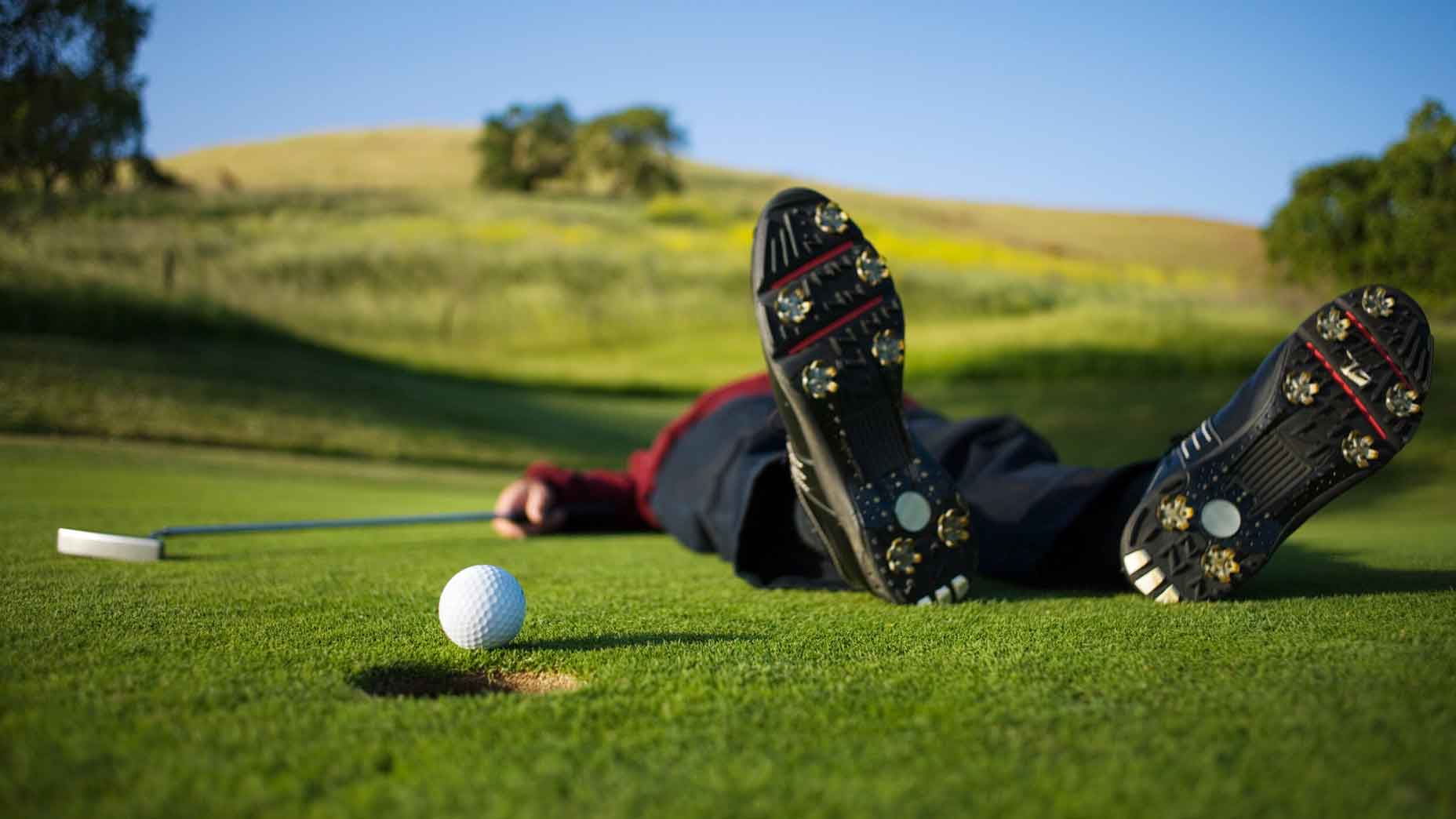 Golfer lies on the green, ball on the edge of the hole