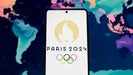 A phone displaying the 2024 Paris Olympics logo in front of a world map.