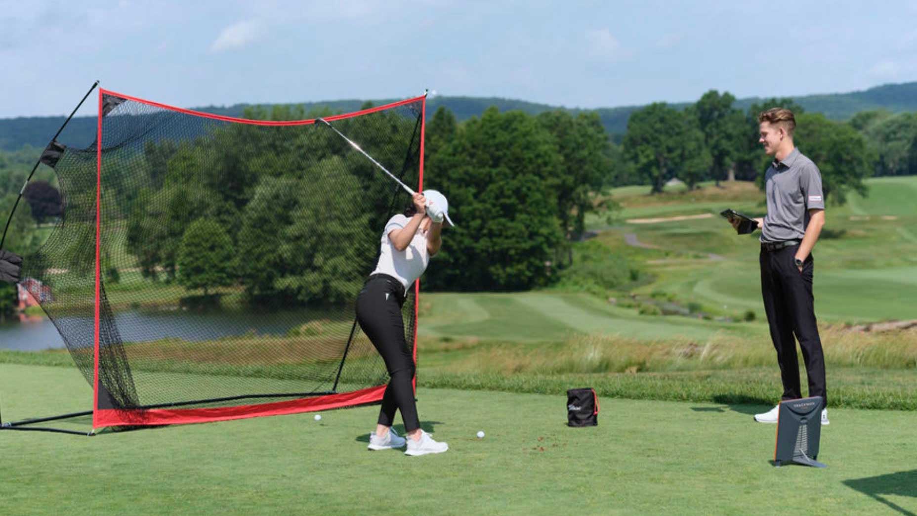Golfer practices hitting into golf net with instructor watching