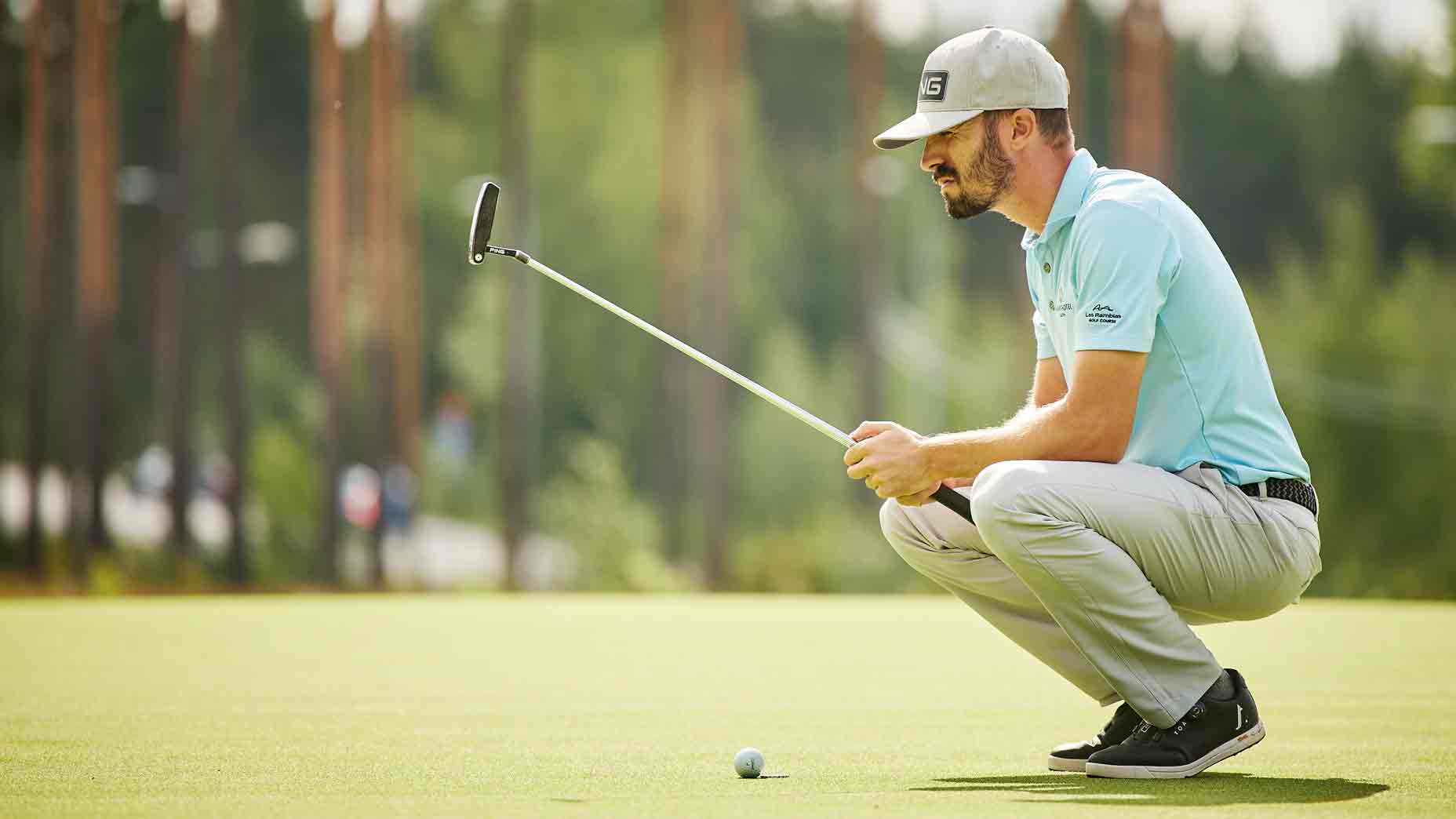 Golfer kneels on golf green to read putt