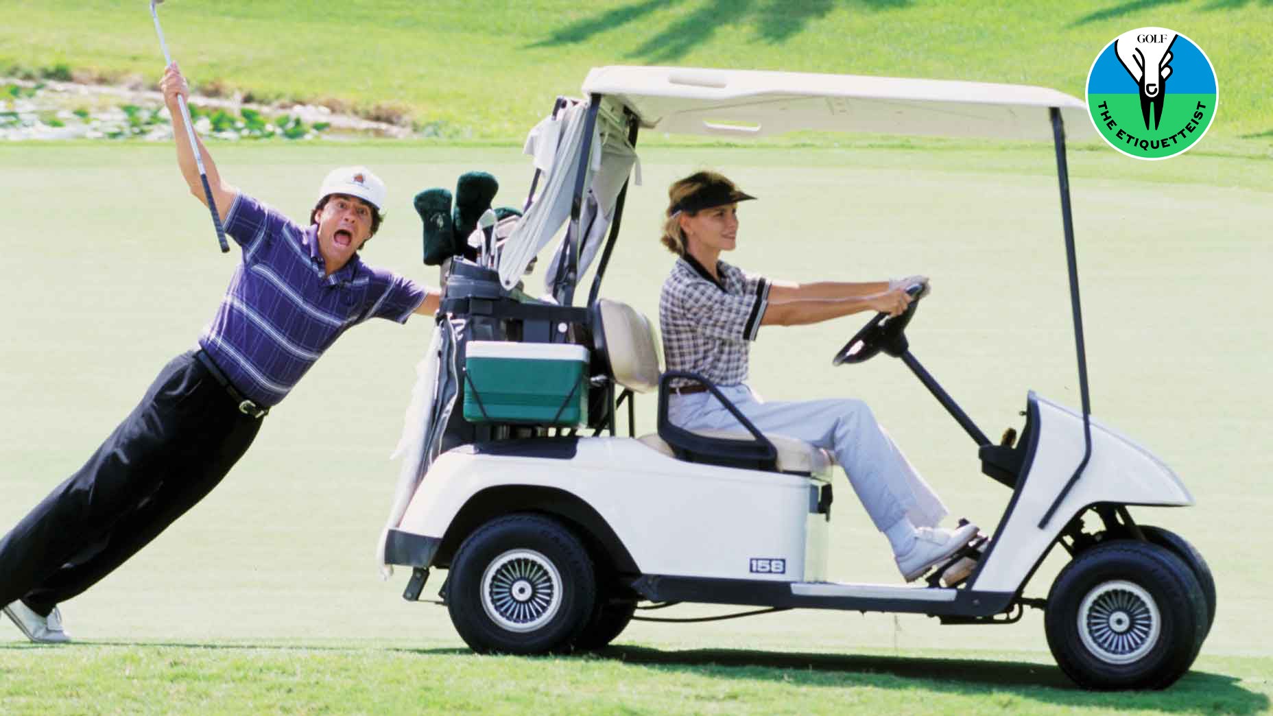 A golfer hanging on to the back of a golf cart.