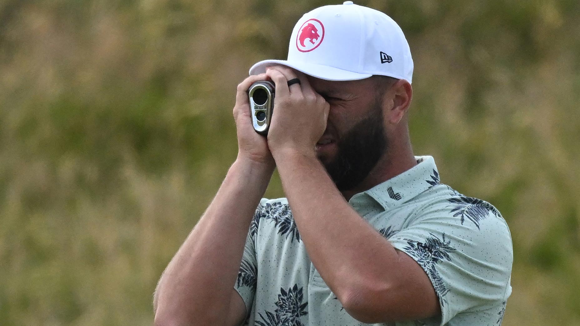 jon rahm looks through rangefinder at the Open Championship in green shirt and white hat