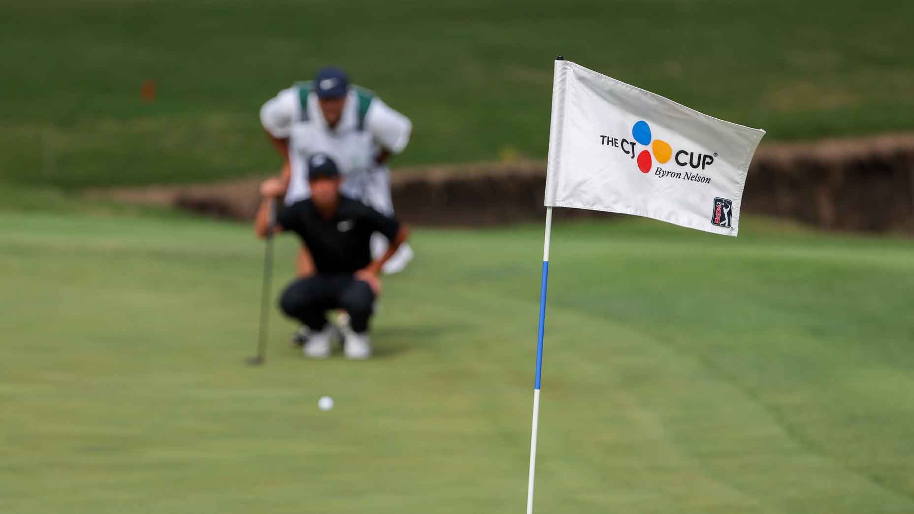 Logo CJ Cup Byron Nelson ditampilkan pada bendera hijau ke-121 dengan Doug Ghim (AS) di latar belakang sedang mengarahkan pukulan putt selama putaran pertama PGA CJ Cup Byron Nelson pada tanggal 2 Mei 2024, di TUP Craig Ranch di McKinney, TX.