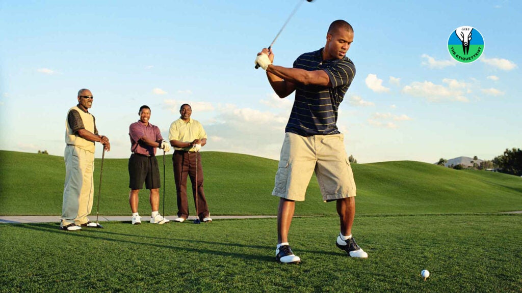 A golfer tees off as his playing partners look on.