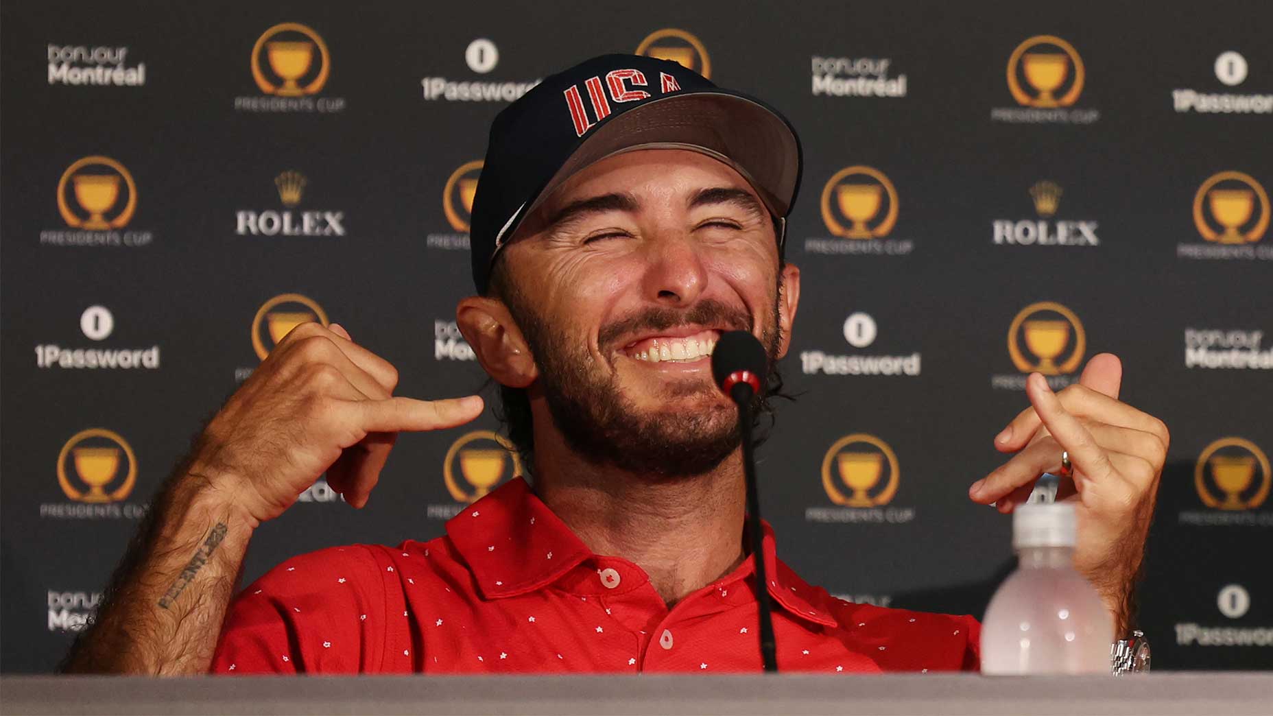 max homa holding a shark in his hand signs at the Presidents Cup victory press conference in a red shirt