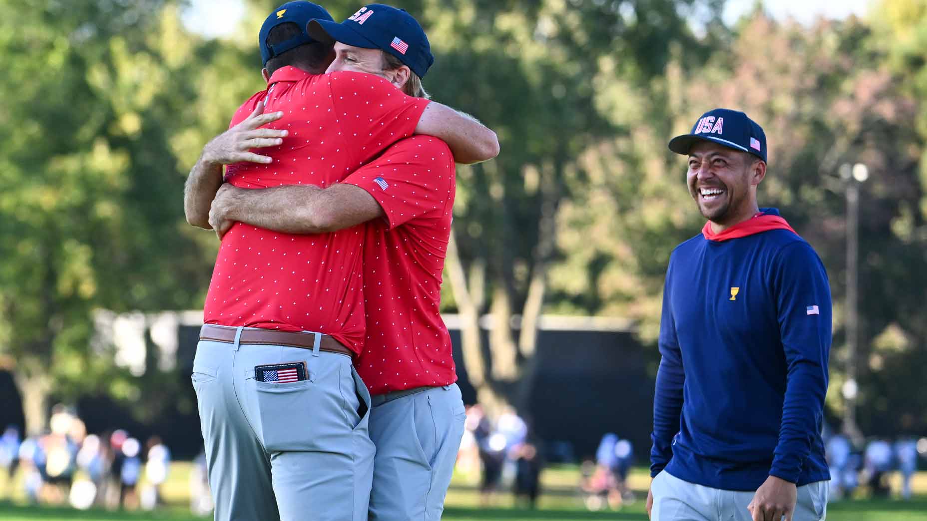 tony finau and russell henley hug while xander schauffele looks on