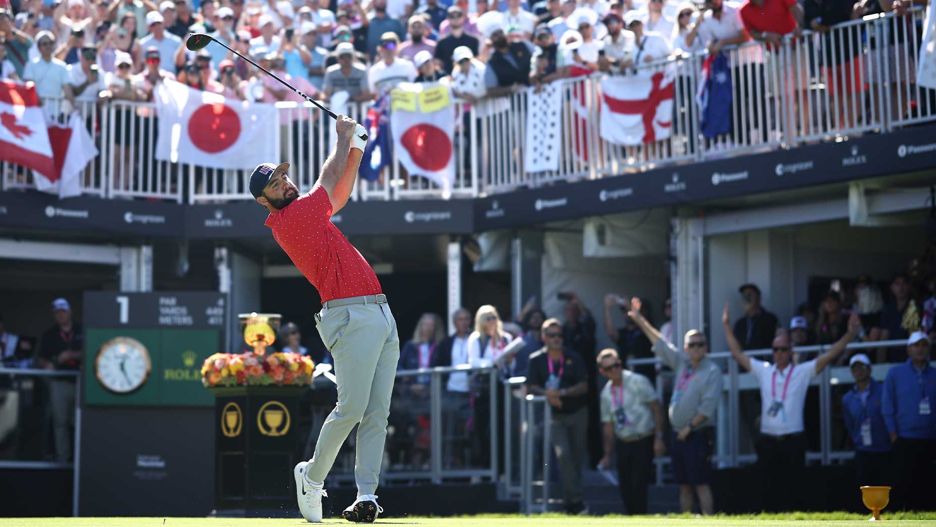 pro golfer scottie scheffler swings driver on the first hole at the 2024 presidents cup in red shirt and gray pants