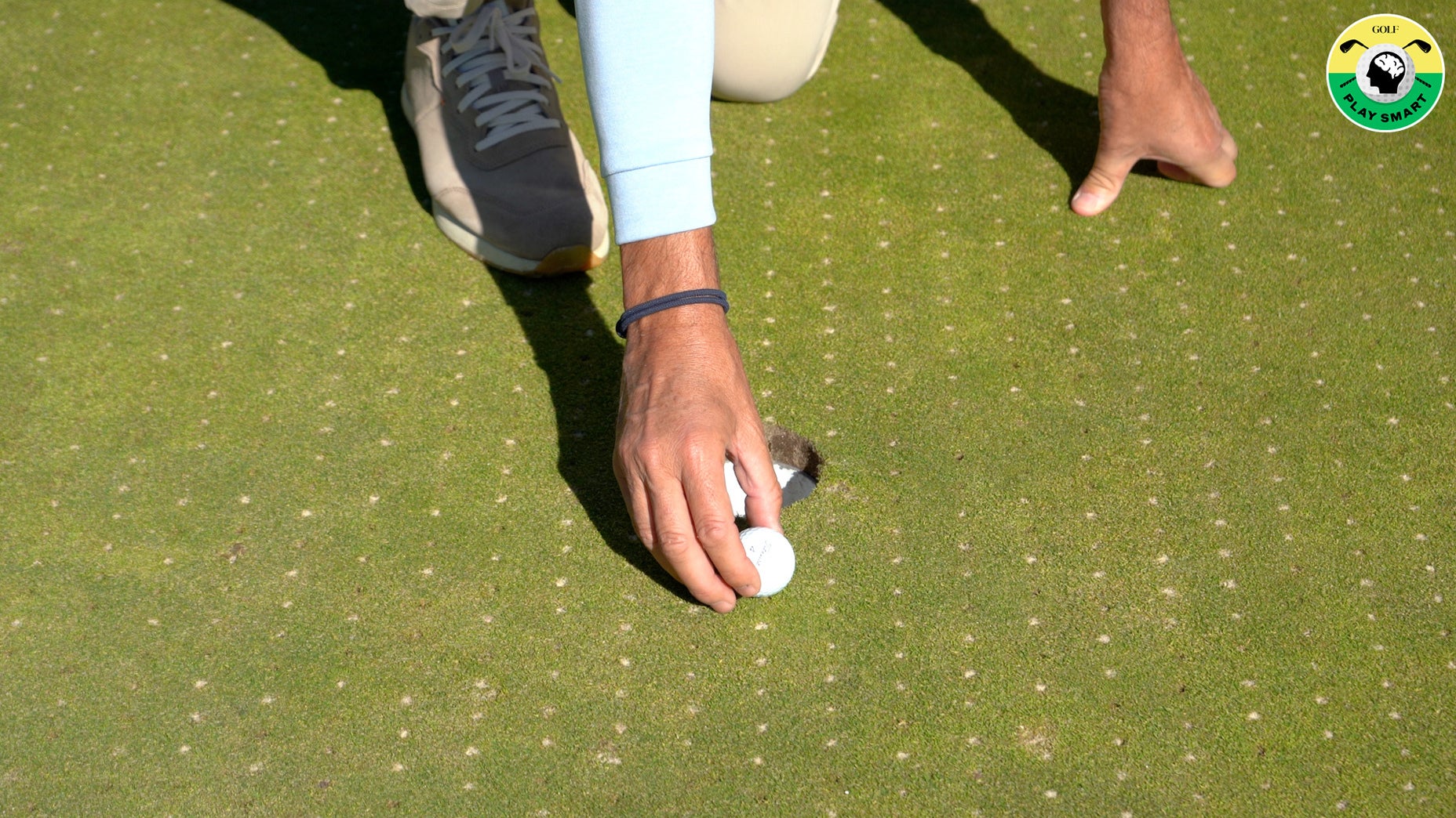 hand holds golf ball in front of hole on green