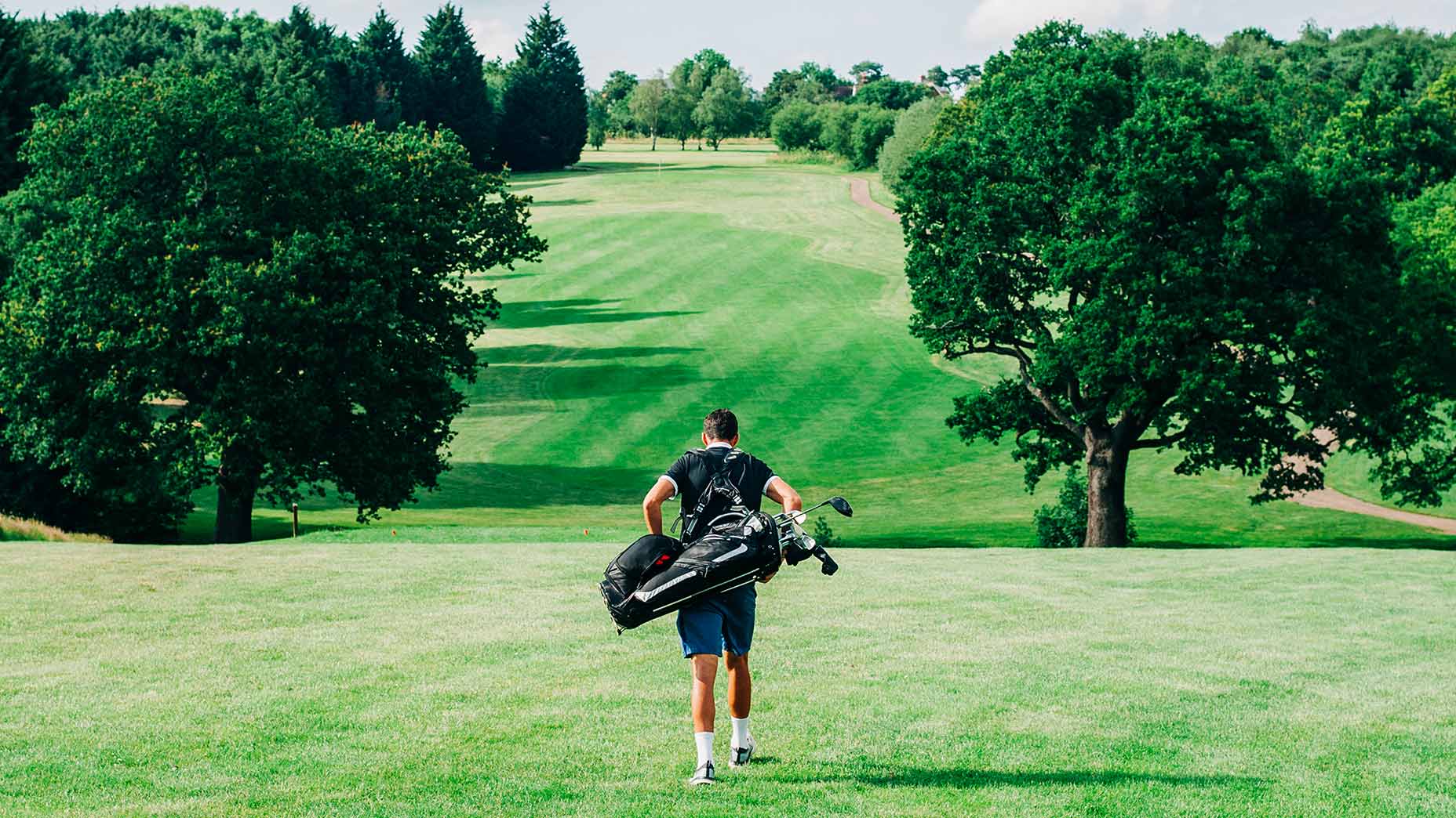 Golfer walks down the middle of a fairway at a golf course