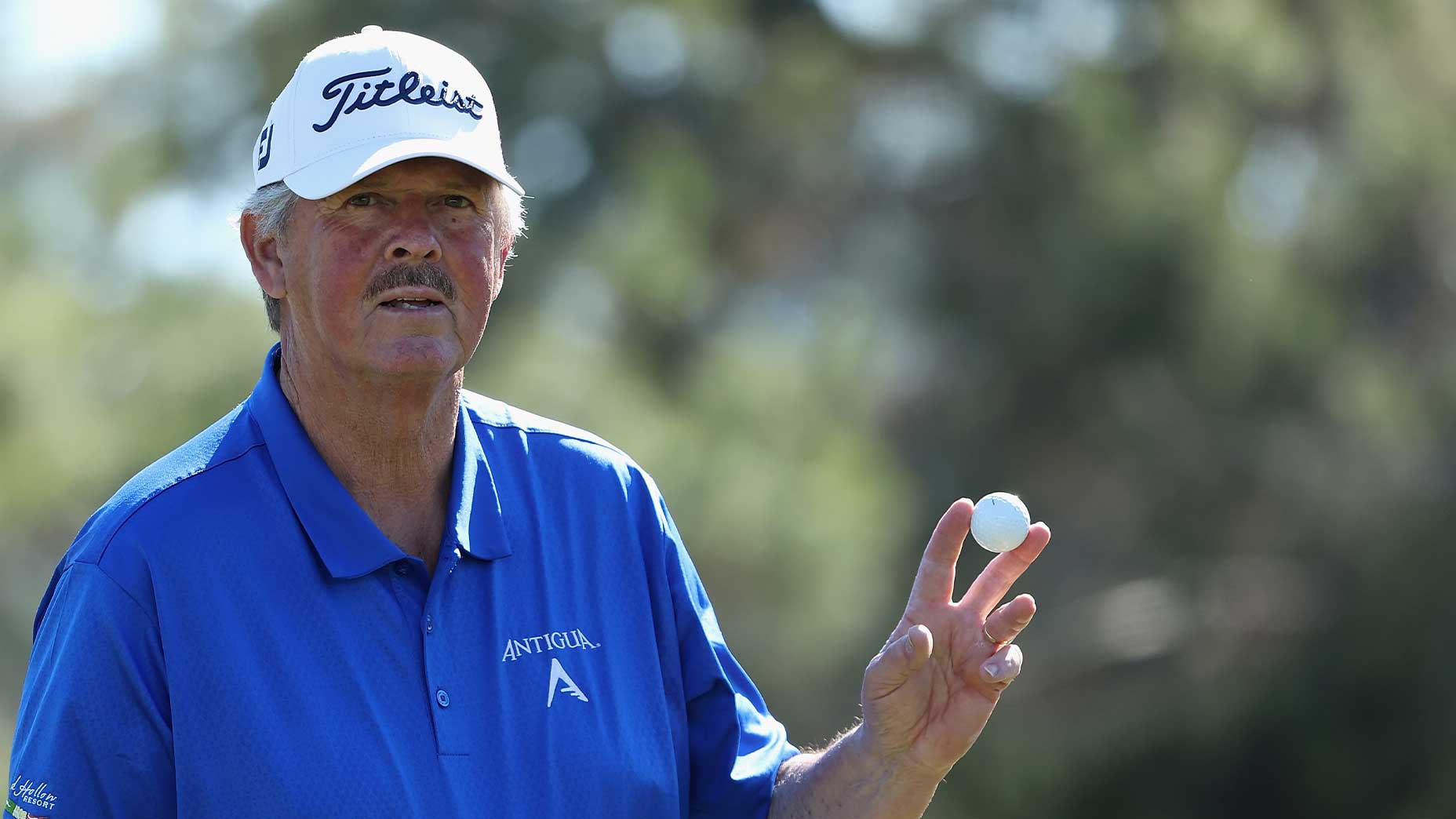 jay don blake waves toward a camera in a blue shirt and white hat