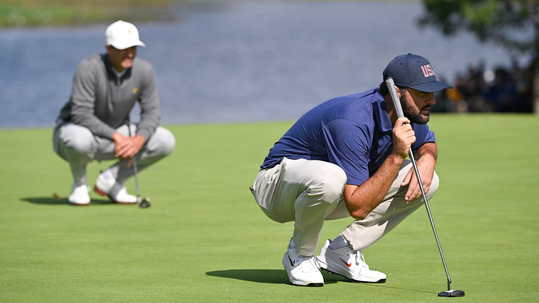 scottie scheffler bends over putt at the presidents cup with adam scott in the background