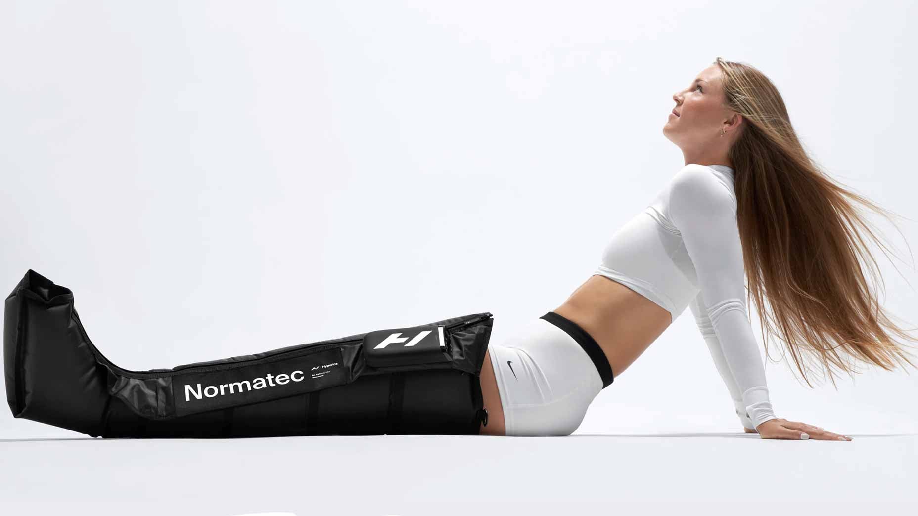 a model sits in normatec compression boots in a white shirt and white shorts