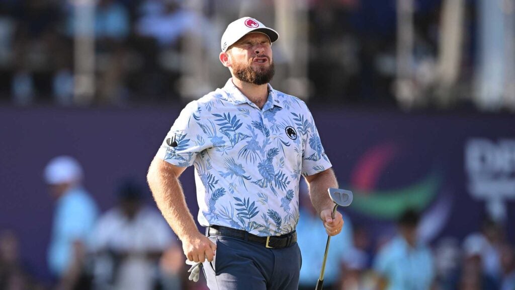 tyrrell hatton grimaces at DP World Tour Championship with putter in hand.