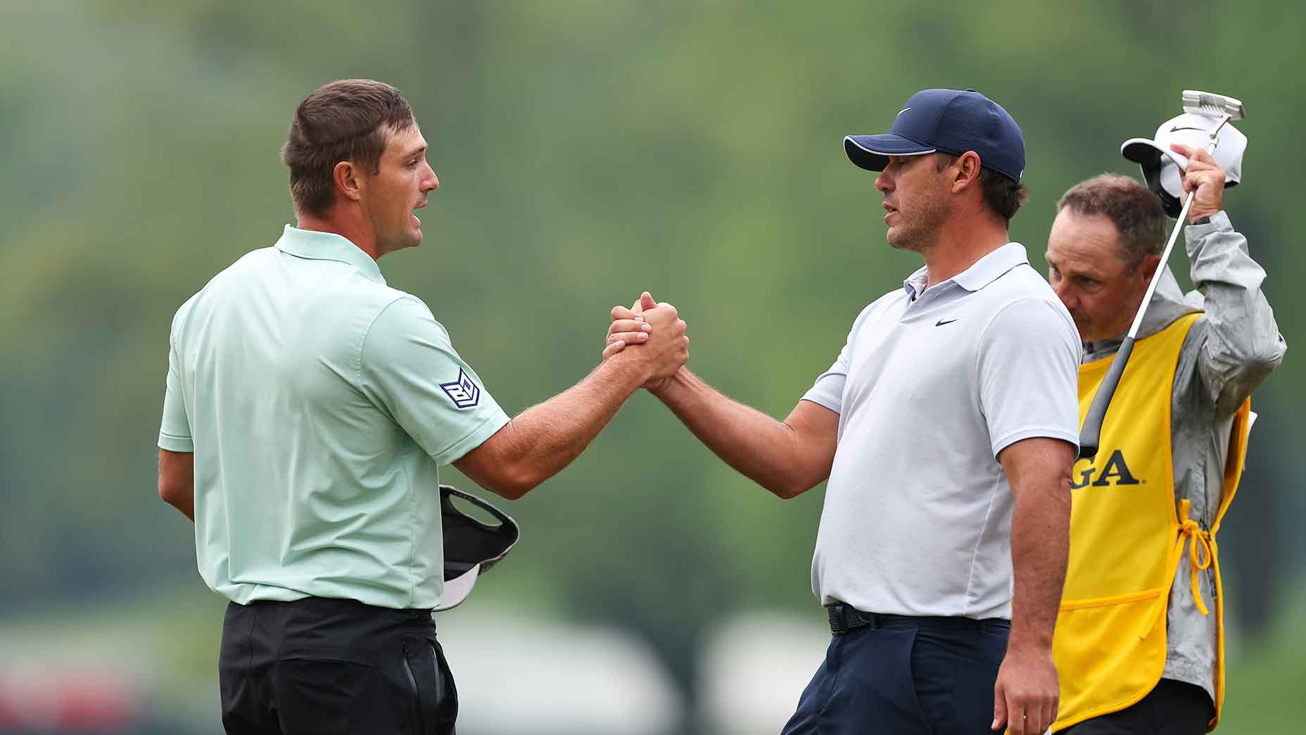 bryson dechambeau in a mint green shirt shakes hands with brooks koepka in a white shirt at the 2023 PGA Championship.