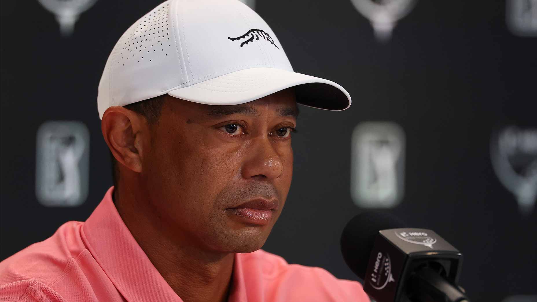 tiger woods stares at hero world challenge press conference in white hat and pink shirt