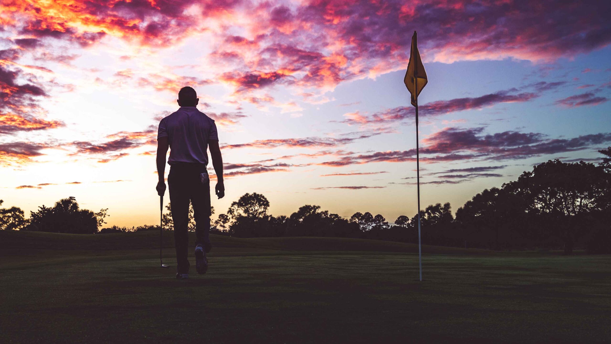 Man golfing under the stunning sky of sunset, walking the green in the silhouette