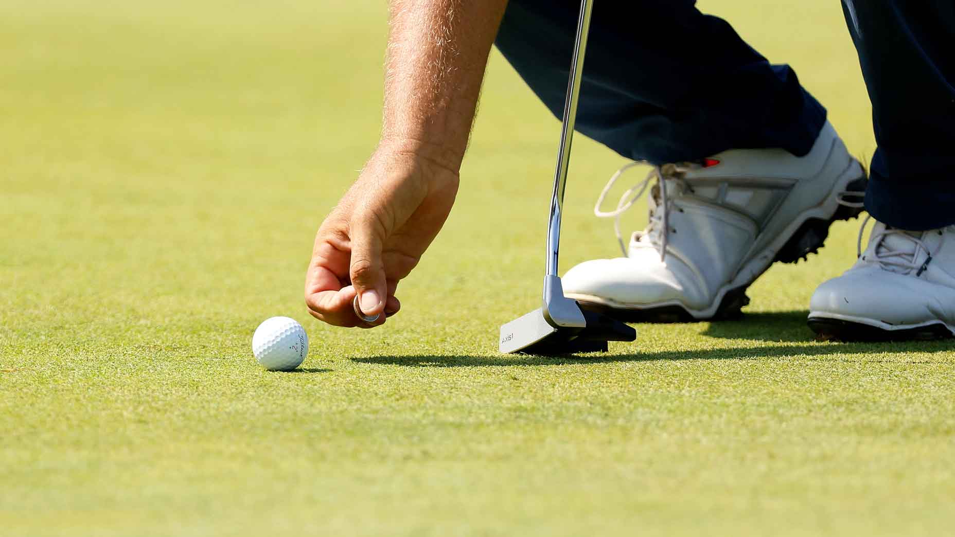 golfer places coin behind golf ball on ground