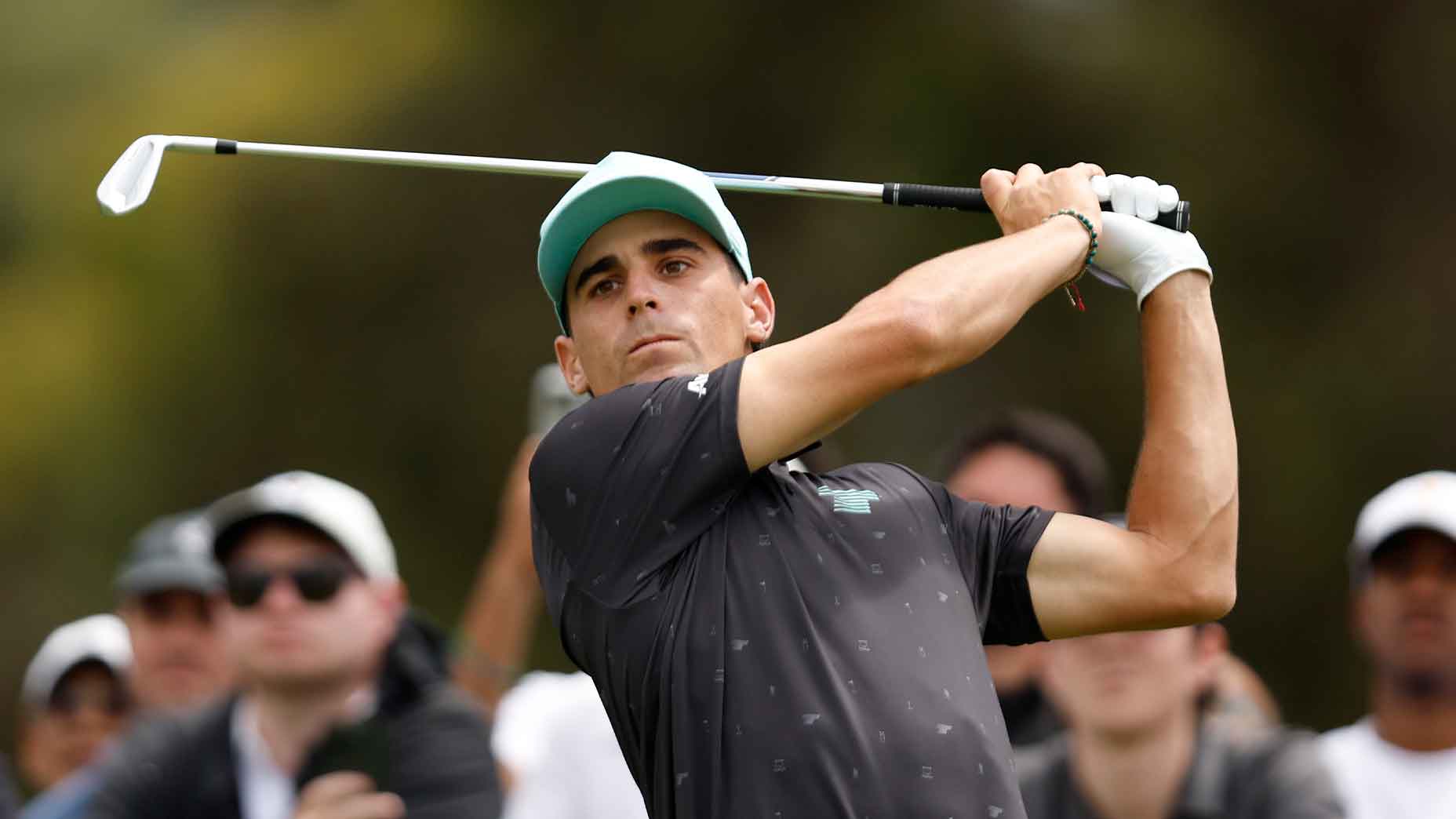 joaquin niemann swings iron in a black shirt at a LIV Golf event in 2024.