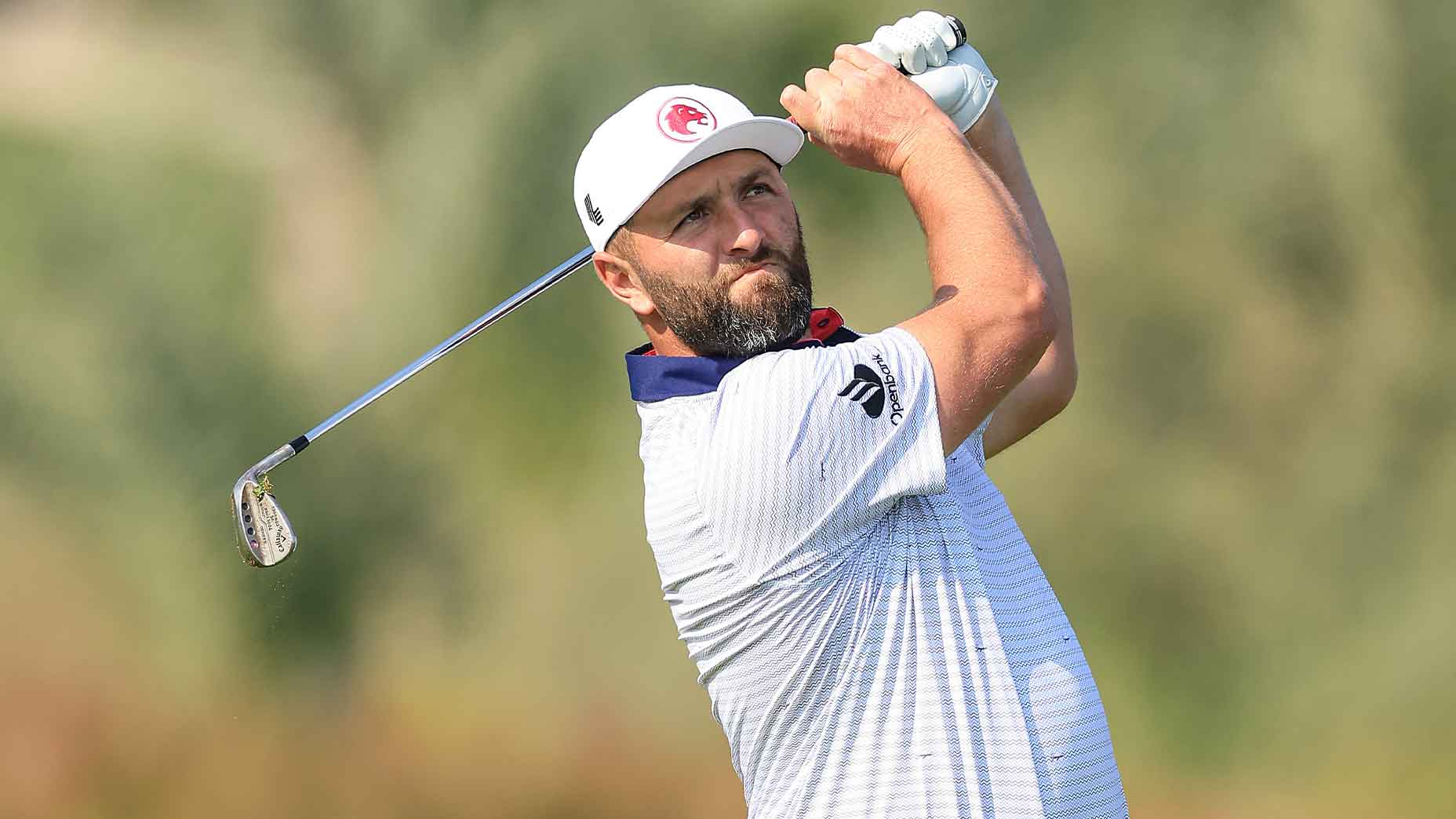 jon rahm swings wedge in LIV Golf shirt and white hat at the Dubai Desert Classic