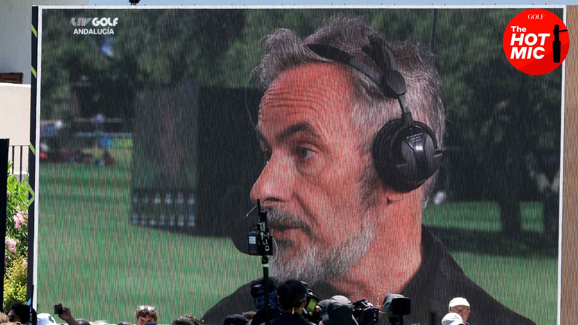 David Feherty, wearing a black shirt, speaks into an on-screen microphone at a LIV golf event