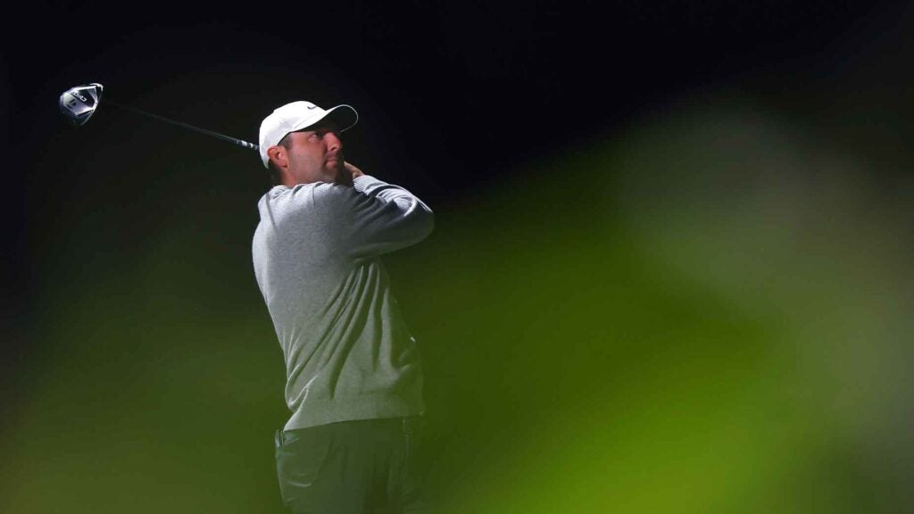 scottie scheffler swings driver at the showdown in vegas wearing a gray sweater and white hat