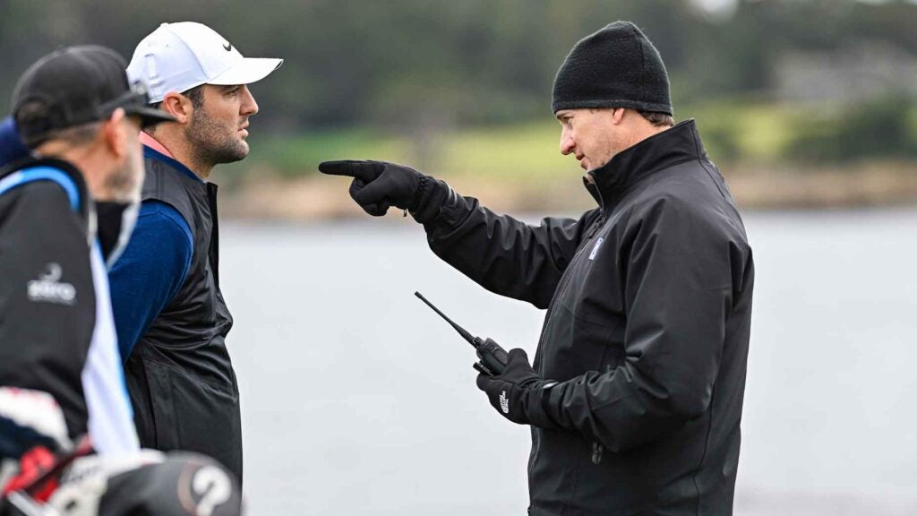 scottie scheffler, in navy sweater, talks to rules official who points back to tee box, with caddie Ted Scott in the background.