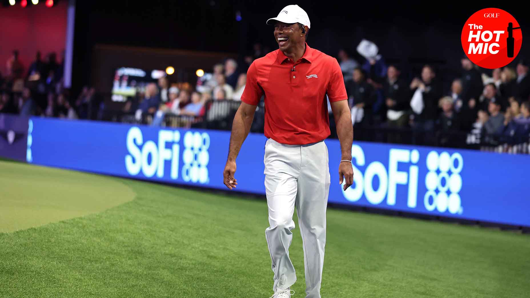 Tiger Woods smiles in a red shirt and white hat during his TGL debut at the Sofi Center in West Palm, Florida.