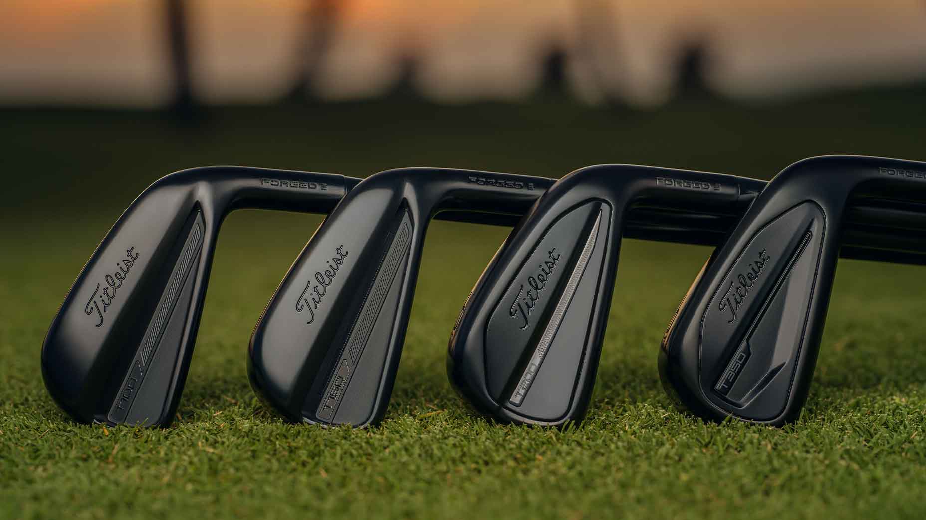 titleist t series black irons stretched across a green lawn with sunset in the horizon