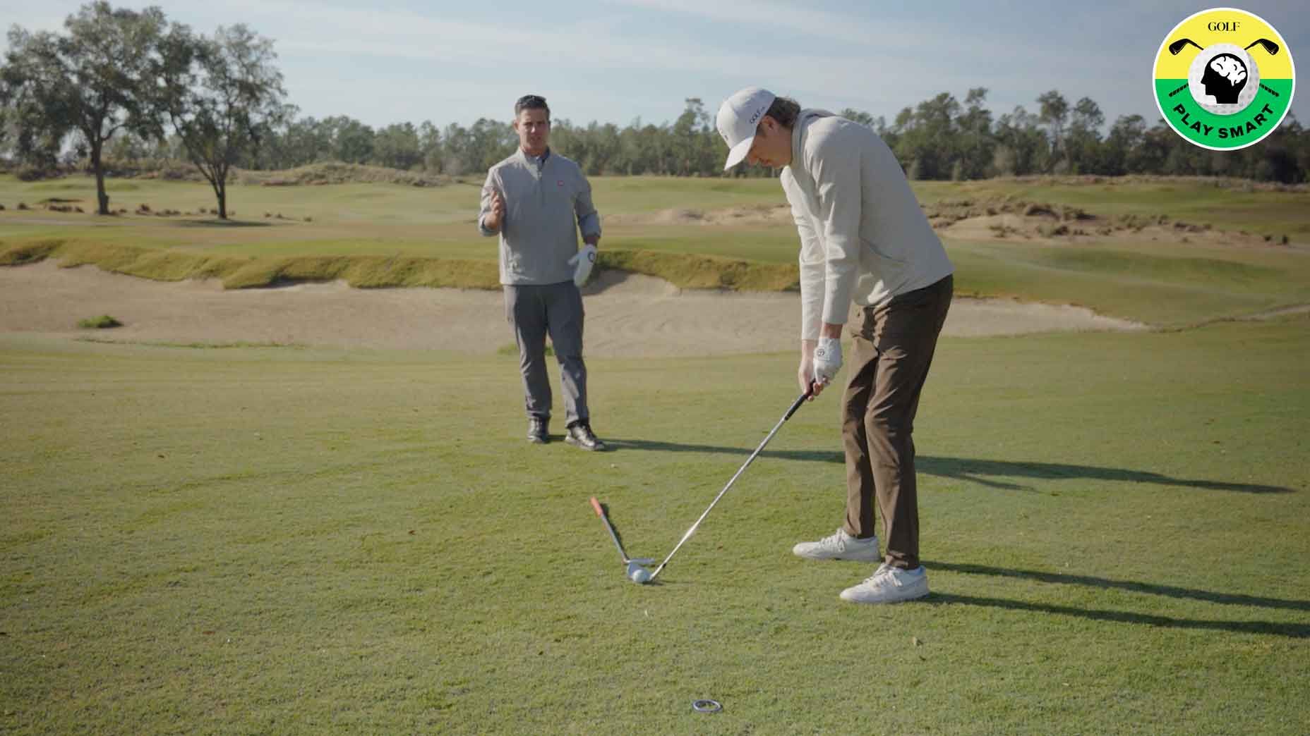 teaches watches as student lines up to hit golf shot