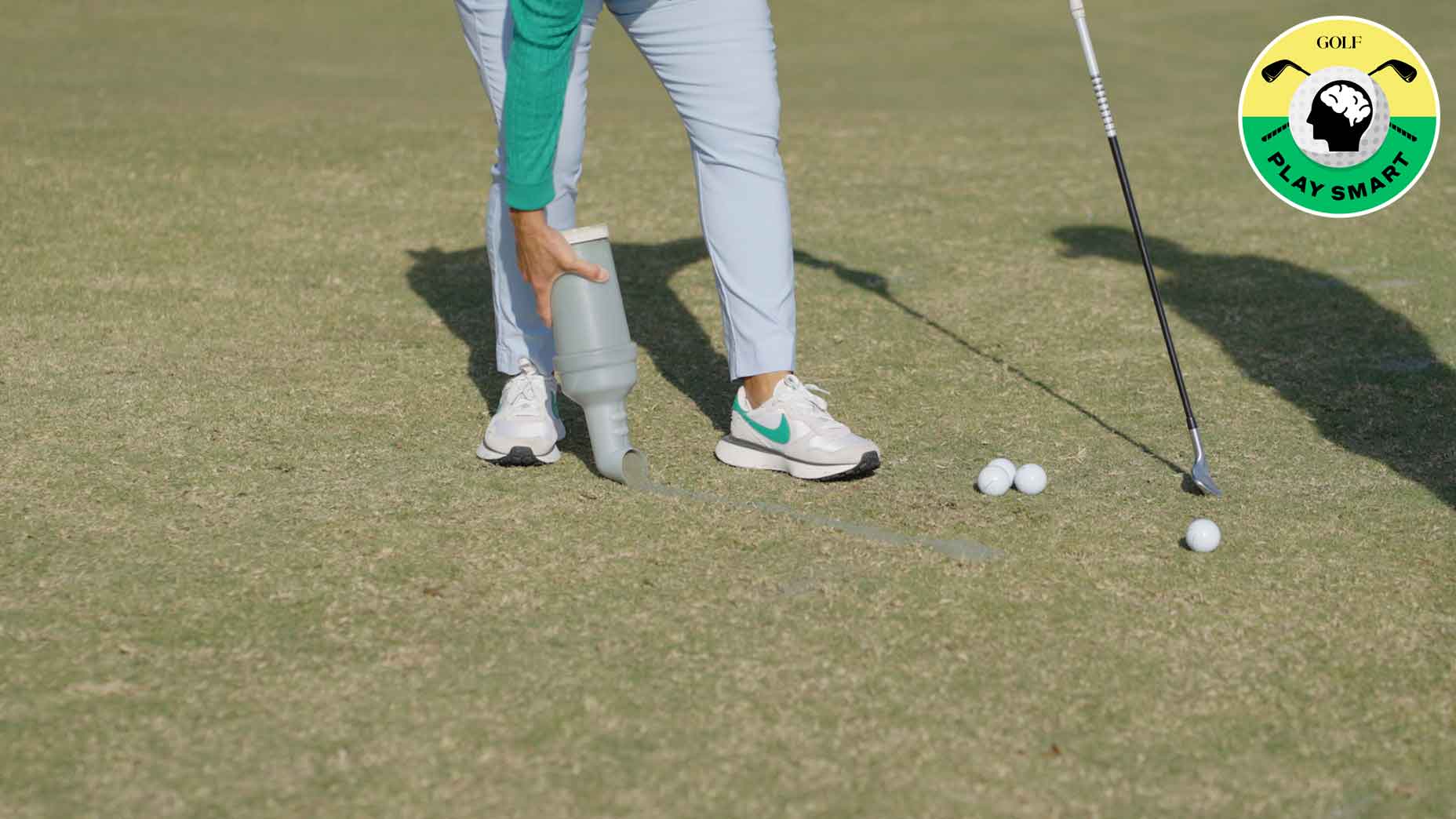 golf balls on the ground with two feet and hand holding sand bottle