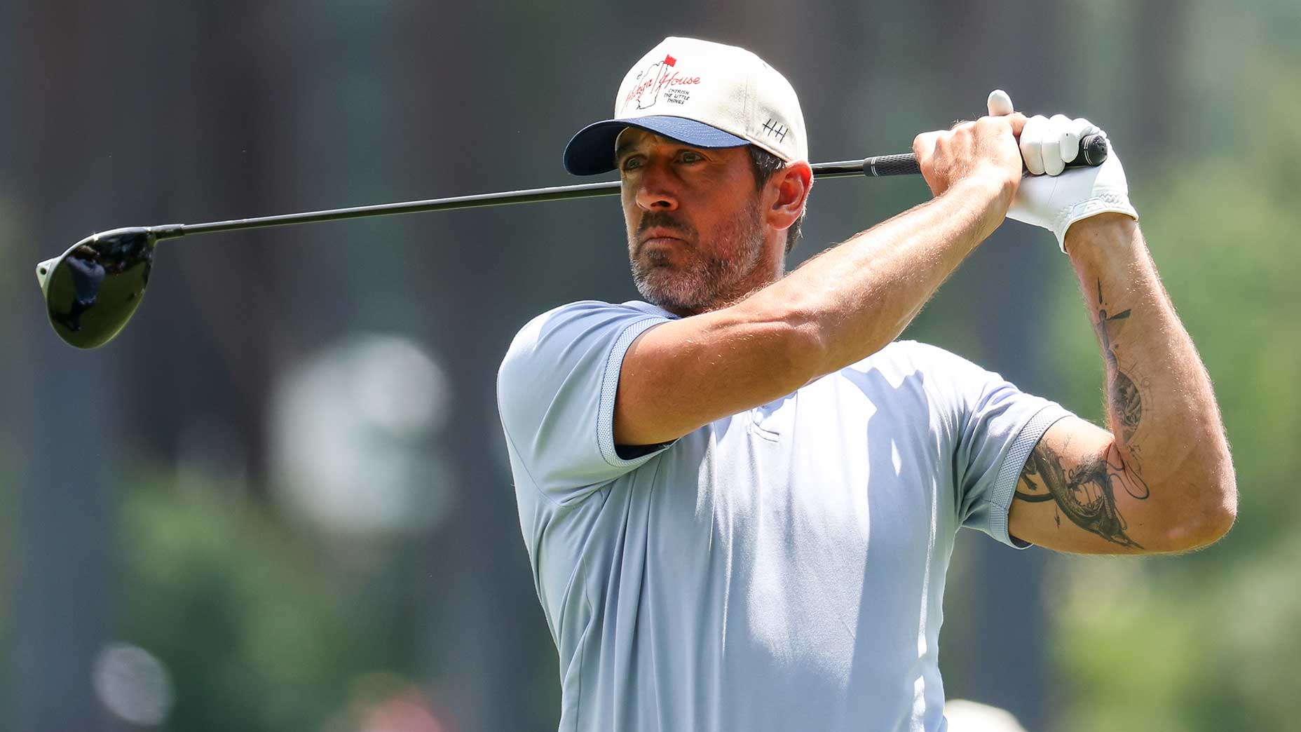 Aaron Rodgers swings a golf club