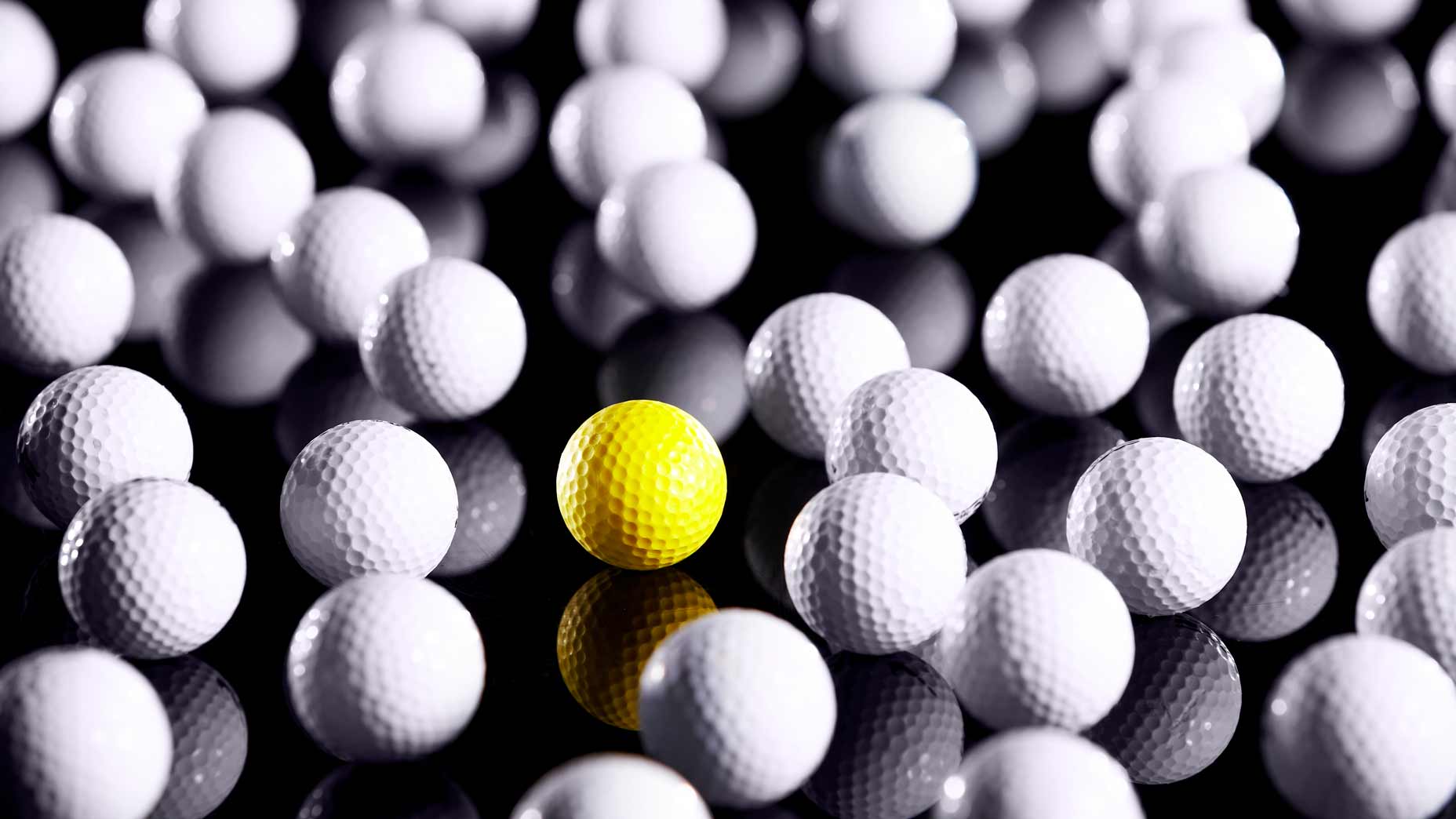 A group of white golf balls with one yellow golf ball, all of which weigh no more than 1.62 ounces.