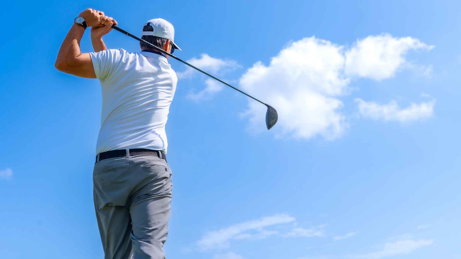 low rear angle of golfer hitting golf ball against a blue sky