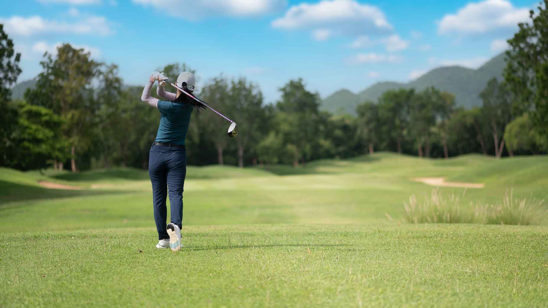 female golfer in blue shirt and navy pants swings golf club