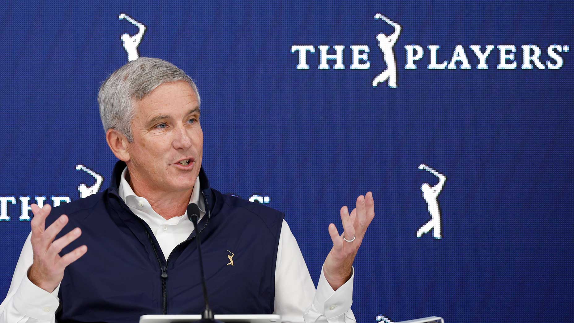 Jay Monahan lifts hands in the player championship with blue vest and white shirt