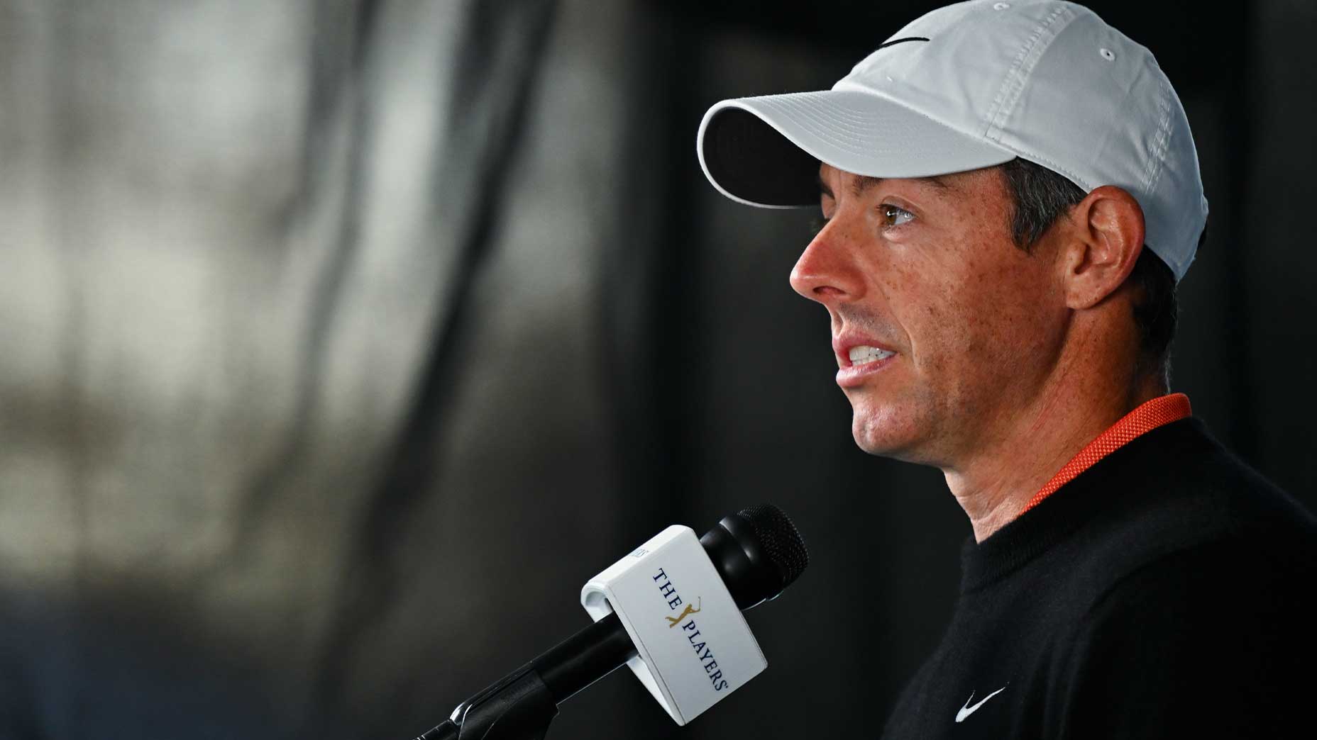 Rory Mcilroy speaks on camera and microphone in white hat and black sweatshirt in player championship