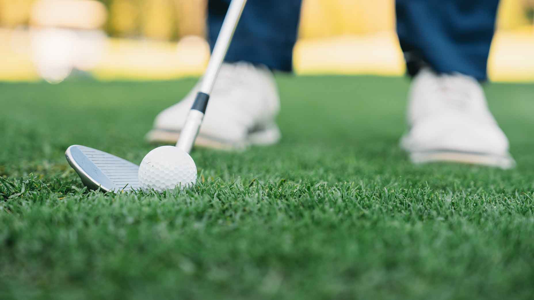 wedge on ground next to ball with white shoes in background