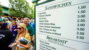 People walk past a vendor sign during a practice round for the 2015 Masters in Augusta, Ga.